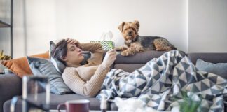 Woman lying sick on sofa with her dog