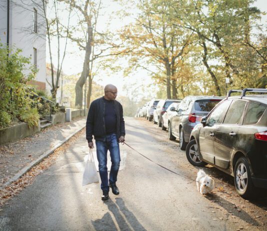 A fit older man walks a small dog white dog down neighborhood streets.