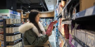 A woman browses for pet food in a grocery store aisle.