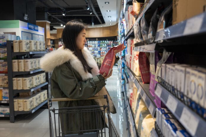 A woman browses for pet food in a grocery store aisle.